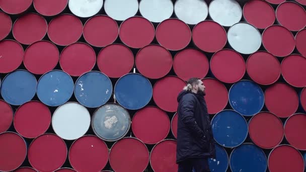 Young bearded guy walks in front of stack of colorful barrels — Stock Video