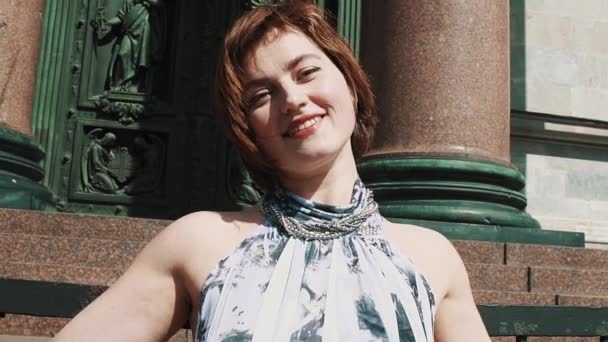 Chica despreocupada en vestido de verano sonriendo delante de la vieja puerta de la iglesia ortodoxa — Vídeo de stock