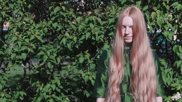 Chica pelirroja de pelo largo de pie cerca del arbusto del parque — Vídeos de Stock