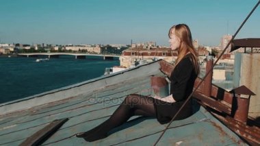 Çatı ile doğal cityscape oturan siyah elbiseli genç ve güzel kadın