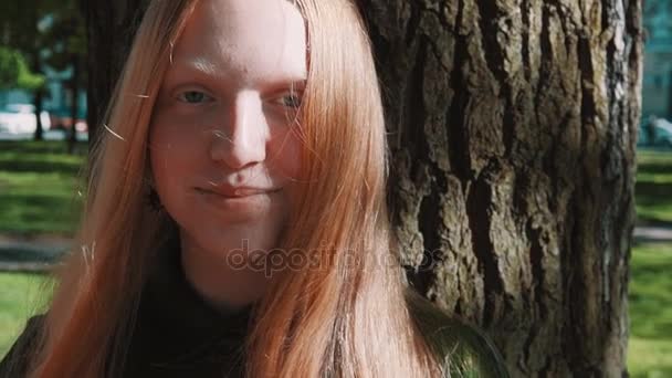 Rousse aux cheveux longs jeune fille debout sous l'arbre du parc — Video