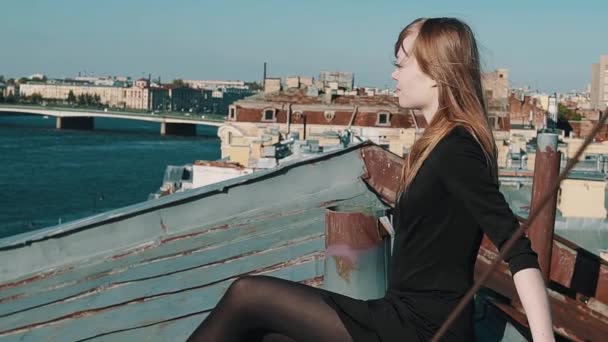 Jovem mulher atraente em vestido preto sentado no telhado com paisagem urbana cênica — Vídeo de Stock