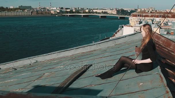 Dość młoda dziewczyna w czarnej sukni siedzi na pokrycia dachowe z malowniczą panoramę miasta — Wideo stockowe
