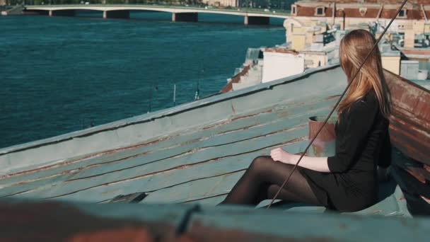 Uroczy młoda dziewczyna w czarnej sukni siedzi na pokrycia dachowe z malowniczą panoramę miasta — Wideo stockowe