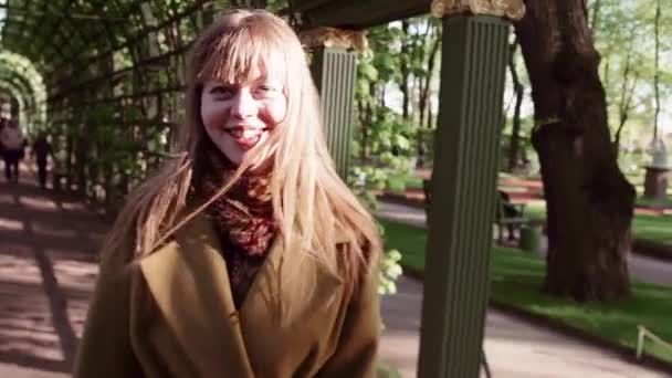 Jolie jeune femme en manteau de laine jaune marchant dans l'allée de l'arche du parc — Video
