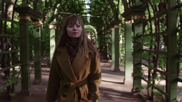 Симпатична молода жінка в жовтому вовняному пальто, що йде в парковій алеї — стокове відео