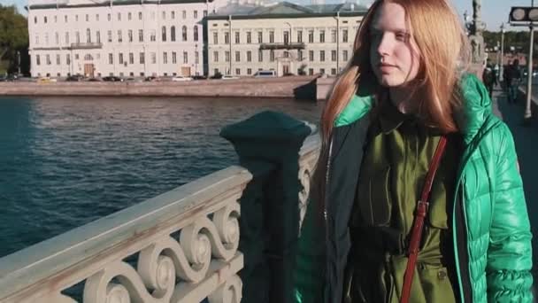 Chica bonita pelirroja de pelo largo caminando a través del puente del río de la ciudad — Vídeos de Stock