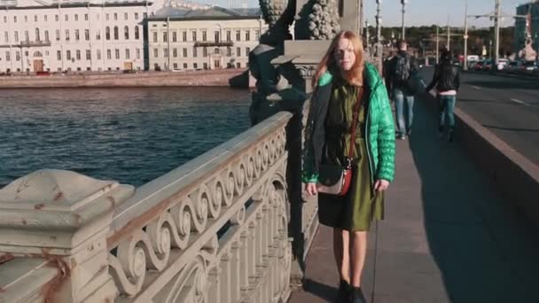 Chica pelirroja de pelo largo caminando a través del puente del río de la ciudad — Vídeos de Stock