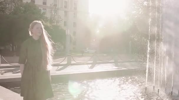 Ung söt rödhårig flicka i grön klänning promenader nära fountain — Stockvideo