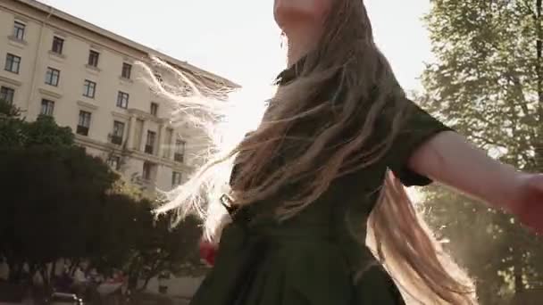 Chica pelirroja bonita de pelo largo en vestido verde girando en la plaza de la ciudad — Vídeos de Stock