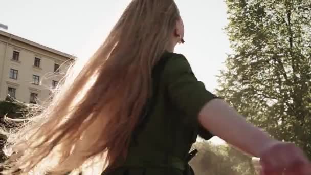Довгошерста гарненька дівчина в зеленому платті, що крутиться на міській площі — стокове відео