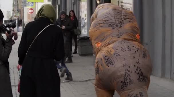 Санкт-Петербург, Російська Федерація - 1 квітня 2017: Людина в костюмі динозавра карбування смішні бездомних дитиною на тротуарі — стокове відео
