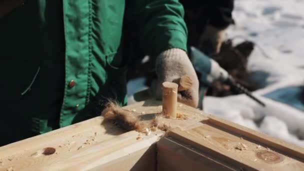 Hand in hameren twee houten balken aan het gat in de houten blok, buiten winter handschoenen — Stockvideo