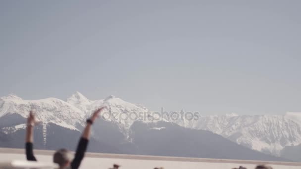 索契, 俄罗斯-2016年3月31日: 白雪皑皑的山脉。在阳光明媚的早晨, 年轻人在户外操场上做瑜伽。举手. — 图库视频影像