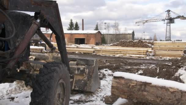 製材所のヤードでの掘削機に雪に覆われた木材の杭が格納されています。 — ストック動画
