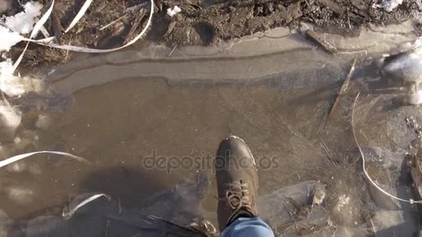 POV person feet in boot breaks ice on muddy puddle — Stock Video