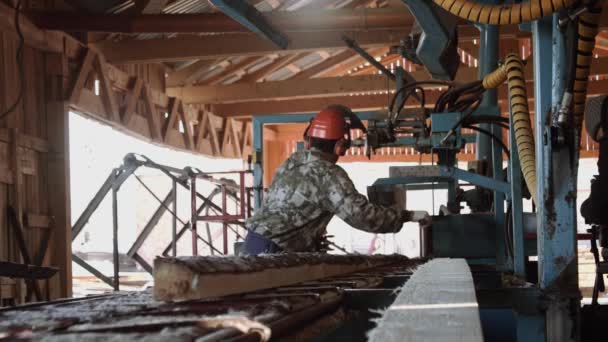 Schrijnwerker in harde hoed snijden hout blok op industriële zag workbench — Stockvideo