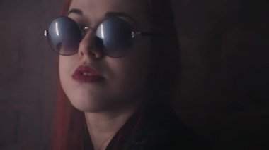 Redhaired kız duvara karanlık odada önünde poz büyük güneş gözlüğü
