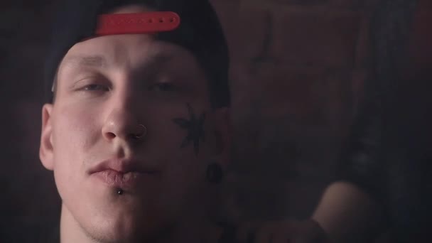 Jeune dur gars dans snapback avec des tatouages de visage en face du mur de briques avec des filles — Video