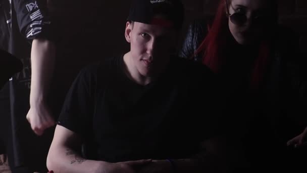 Молодой преступник в шапочке с татуировками на лице перед кирпичной стеной с девушками — стоковое видео