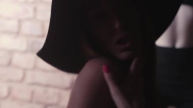 Karanlık odada, kırmızı tuğla duvar hareketleri alay şapkalı seksi genç kadın