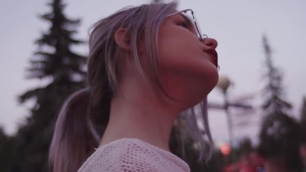 Menina loira atraente com rabo de cavalo em óculos redondos no parque de diversões — Vídeo de Stock