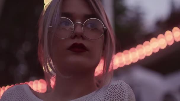 Hermosa chica rubia con cola de caballo en gafas redondas en el parque de atracciones — Vídeos de Stock