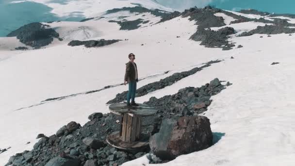 Aerial skott man sprida armar står på kabel spolen på klipporna vid snötäckta berg — Stockvideo