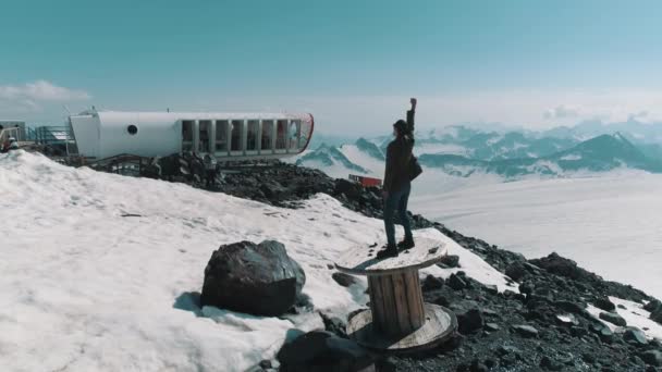 Zdjęcia lotnicze mężczyzna stojący doping na szpuli przewodu na skały na ośnieżonych gór — Wideo stockowe