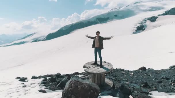 Flygfoto man sprida armar står på kabel spolen på klipporna vid snötäckta berg — Stockvideo