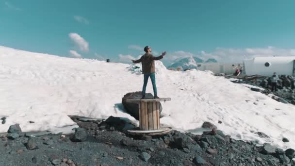 Vue aérienne homme lève les bras debout sur la bobine de câble sur les rochers dans les montagnes enneigées — Video