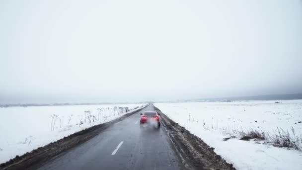 El coche del músculo rojo comienza a conducir en la carretera rodeada de campos cubiertos de nieve — Vídeo de stock