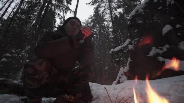 Viajante cara sentado na floresta na frente da fogueira tenta se aquecer — Vídeo de Stock