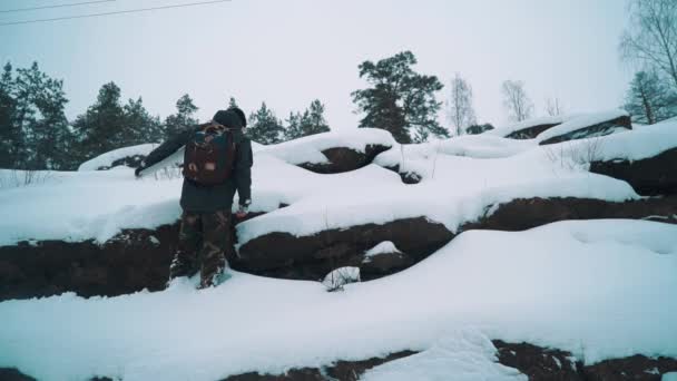 Jovem escalando penhasco rochoso lado coberto de neve — Vídeo de Stock