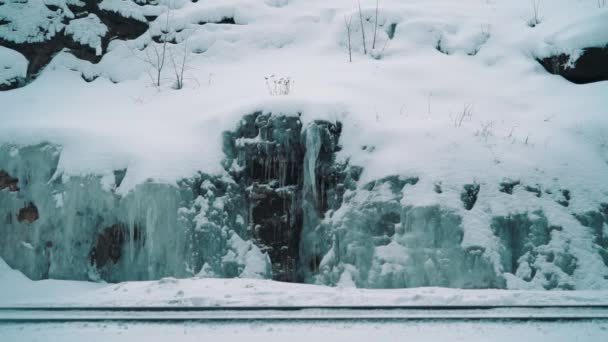 Giovane uomo che cammina sul sentiero ferroviario lungo la scogliera di montagna coperta di ghiaccio — Video Stock