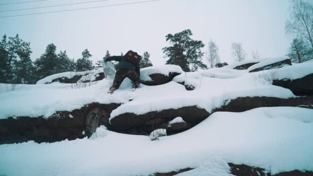 Young traveler climbing rocky cliff side covered in snow — Stock Video