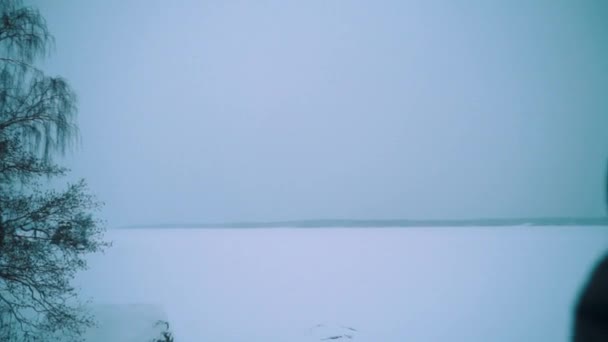 バックパック立っている雪の上で若い男は冬の日の湖の岸をカバー — ストック動画