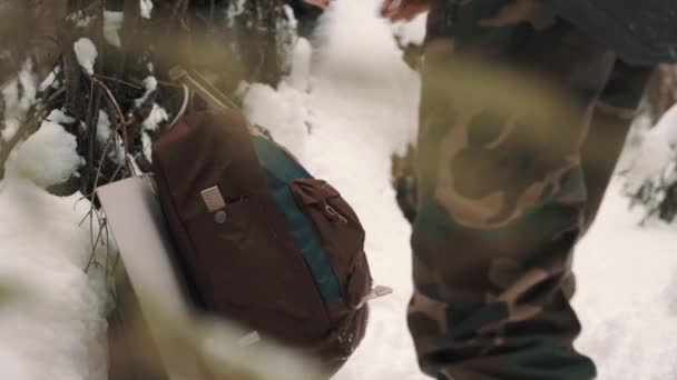 Man in camouflage pants picks up backpack and puts on forest pathway — Stock Video