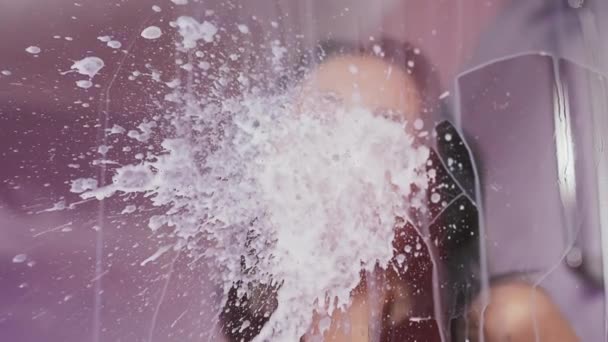 Sexy chica joven en cabina de ducha escupe leche sobre vidrio — Vídeo de stock