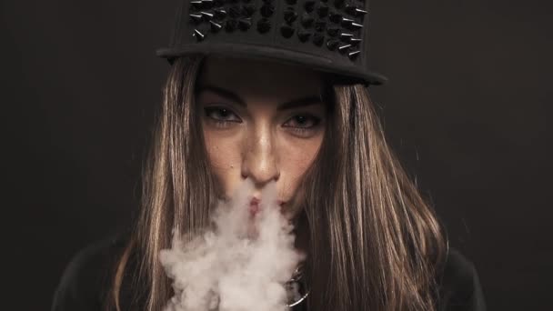 Young attractive girl in spiked snapback cap blows vape smoke out nose — Stock Video