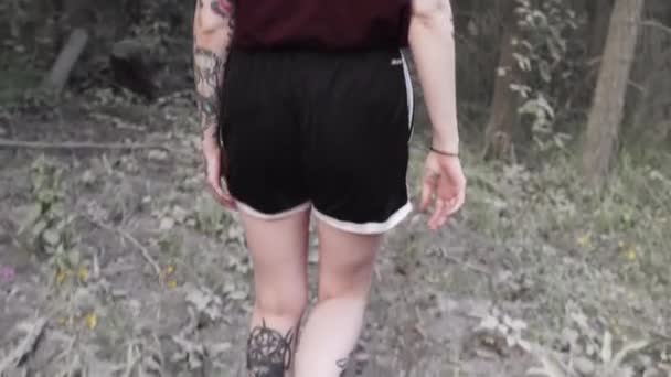 Joven chica punk tatuada caminando sobre hojas cubiertas camino en los bosques — Vídeo de stock