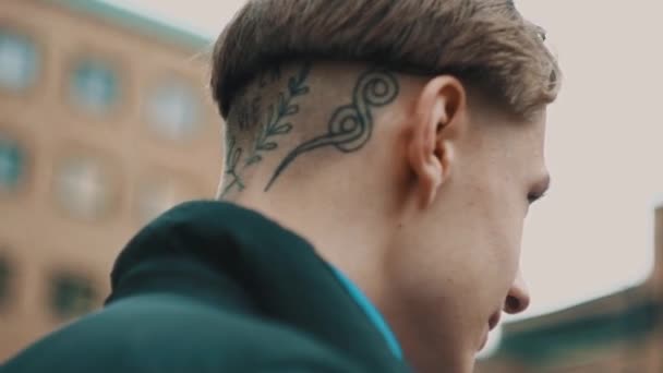 Портрет стильного молодого парня с татуировкой на затылке за пределами современного здания — стоковое видео