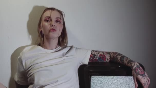 Punk tattooed girl sitting near working static tv set in dark room — Stock Video