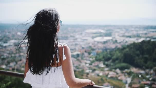 Jovem mulher de vestido branco em pé na varanda da villa olhando para a cidade — Vídeo de Stock