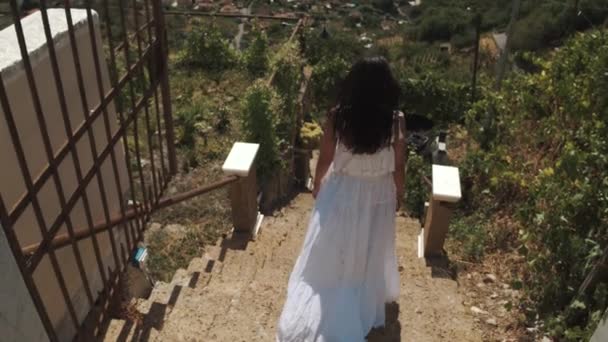 Chica joven en vestido blanco de pie caminando escaleras de villa en las montañas — Vídeo de stock