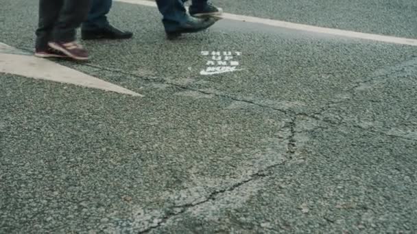 Pies de personas caminando sobre asfalto mojado con marcaje vial — Vídeo de stock