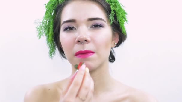 Jong meisje met groene peterselie op hoofd, eet staart van aardbeien. Poseren op camera — Stockvideo
