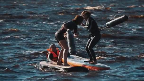 Two women in life vests fighting with soft bats surfing boards in water — Stock Video