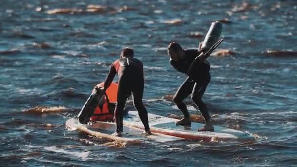 Two men fighting with rolled mats standing on surfing board in wavy water — Stock Video