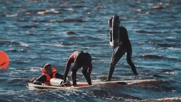 Dos tipos peleando con esteras enrolladas de pie sobre tabla de surf en agua ondulada — Vídeo de stock